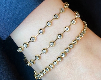 May include: Three gold bracelets with small round clear stones. The bracelets are layered on a person's wrist.