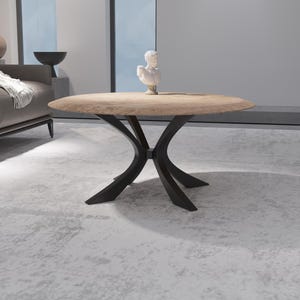 May include: A contemporary coffee table featuring a circular, light-toned wooden surface and a black, geometric base. The table is about 100 cm in diameter and is in a living room. A small white bust is placed on top.