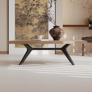 May include: A contemporary living room with a light wood coffee table with black legs, a large framed artwork, and a decorative vase with dried branches. The room has a minimalist design with neutral tones.