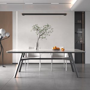 May include: A modern dining room scene featuring a rectangular table with a white surface and dark gray legs. Two white chairs are positioned on each side. A vase with greenery and a bowl of oranges are on the table.