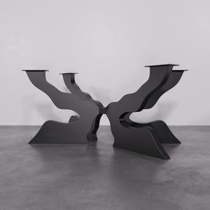 Op de afbeelding: Zwarte metalen tafelpoot met een uniek, abstract ontwerp. De poot heeft een breed, plat bovenblad en vier poten die in een organische vorm buigen en draaien.