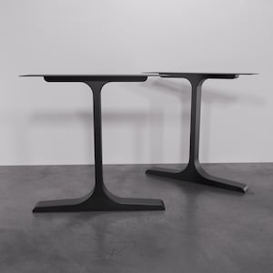 Könnte beinhalten: Zwei schwarze Tischbeine aus Metall mit einem einzigartigen T-förmigen Design. Die Beine sind aus robustem Metall gefertigt und haben ein elegantes, modernes Aussehen.