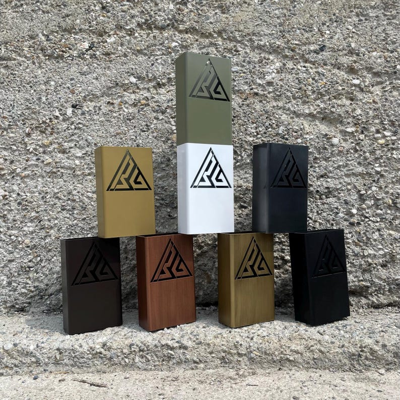May include: A collection of rectangular boxes in various colors, including olive green, white, black, and gold. Each box features a triangular logo cut out on the front. The boxes are arranged in a visually appealing display.