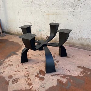 May include: Black metal table base with five legs that curve upwards and connect at the top. The base has a starburst design.