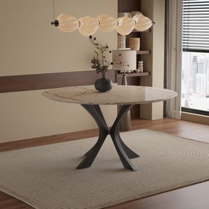 May include: A circular marble dining table with a dark grey metal base, set on a light beige rug. A vase with decorative branches sits on the table. A light fixture hangs above the table.