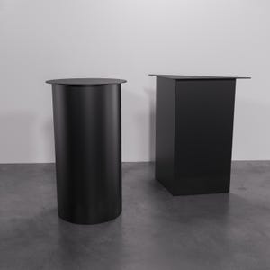 May include: Two black display stands, one round and one square, made of a smooth, matte material. The round stand is taller than the square stand.