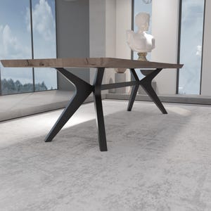 May include: A modern dining table with a light brown wooden top and black metal legs. The table has a unique, angular design. The legs are angled and cross each other for support. The table is in a well-lit room with large windows.