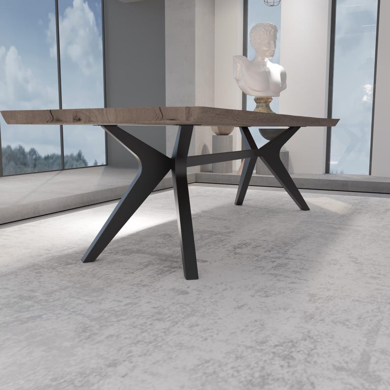 May include: A modern dining table with a light brown wooden top and black metal legs. The table has a unique, angular design. The legs are angled and cross each other for support. The table is in a well-lit room with large windows.