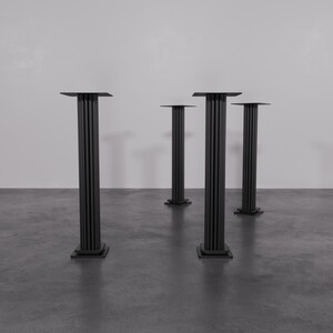 May include: Four black metal table bases with a fluted column design. The bases are square and have a flat top surface.
