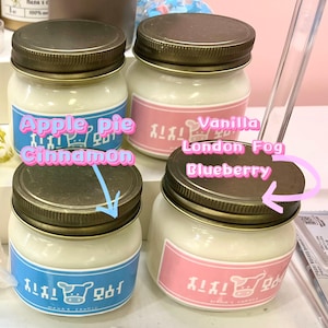 Puede incluir: Cuatro velas en tarros de vidrio con tapas de metal. Las etiquetas dicen "Apple Pie Cinnamon", "Vanilla London Fog" y "Blueberry". Los tarros tienen una vela blanca en su interior y est&aacute;n sobre una superficie blanca.