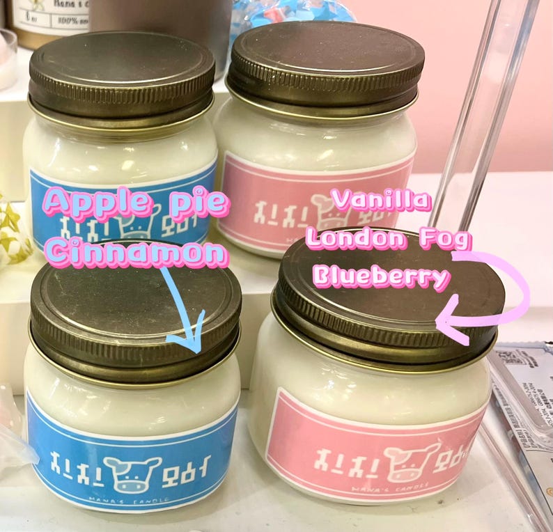 Puede incluir: Cuatro velas en tarros de vidrio con tapas de metal. Las etiquetas dicen "Apple Pie Cinnamon", "Vanilla London Fog" y "Blueberry". Los tarros tienen una vela blanca en su interior y est&aacute;n sobre una superficie blanca.