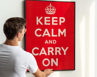 Può includere: Un poster rosso incorniciato con le parole bianche "KEEP CALM AND CARRY ON" e una grafica a corona bianca. La persona che tiene il poster indossa una maglietta bianca.