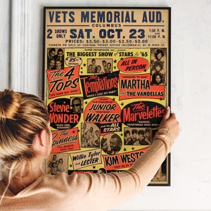 May include: A framed vintage concert poster for a show at Vets Memorial Auditorium in Columbus, Ohio, featuring The Temptations, Stevie Wonder, and more. The poster is in black, red, yellow, and white, with the text "The Biggest Show of Stars for '65".