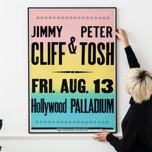 May include: A vintage concert poster with a pink, yellow, and blue gradient background. The poster advertises a concert featuring Jimmy Cliff and Peter Tosh on Friday, August 13th at the Hollywood Palladium.