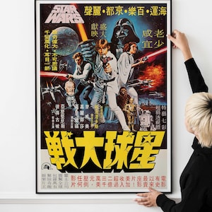 May include: A framed Star Wars film poster with Japanese text. The poster features Luke Skywalker, Darth Vader, and Princess Leia. The background is a mix of blue, orange, and black, with various space battle scenes.