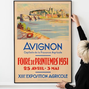 May include: A vintage travel poster advertising the Avignon Spring Fair in 1931. The poster features a colorful illustration of the city of Avignon, France, with the Rhone River in the foreground. The text on the poster reads "Avignon, Capitale de la Provence Agricole, Foire de Printemps 1931, 25 Avril - 3 Mai, XIIIe Exposition Agricole."
