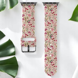 May include: Two-piece floral watch strap with a light beige background and a pattern of small pink and red flowers. The strap has a silver-coloured buckle and connectors. The watch strap is displayed on a white surface with green leaves.
