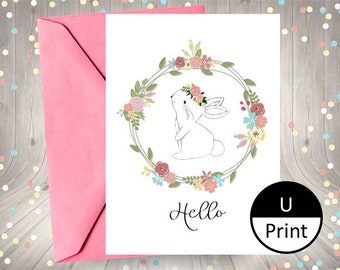 May include: A white bunny with a floral crown sits inside a wreath of colorful flowers. The text "Hello" is written below the bunny. The image has a white background and a pink envelope.