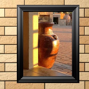 Puede incluir: Un gran jarrón de barro de color terracota se encuentra en una puerta, enmarcado por una ventana negra. El jarrón es redondo y tiene una amplia abertura en la parte superior. La puerta está hecha de ladrillo y tiene un suelo de piedra. El sol brilla a través de la puerta, proyectando un cálido resplandor sobre el jarrón.