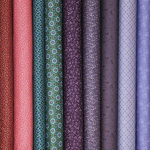 May include: A collection of fabric rolls in various colors and patterns. The fabrics include floral, paisley, and geometric designs in shades of red, pink, teal, green, purple, and lavender. The rolls are tightly wound, showcasing the variety of textures and prints.