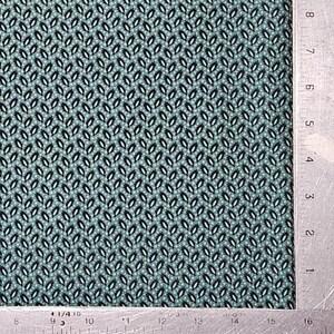 May include: Close-up of a fabric with a repeating pattern of small, dark blue and white leaf-like shapes on a light teal background. The pattern is arranged in a diagonal grid. A metal ruler is on the right side of the fabric.