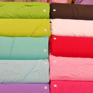 Op de afbeelding: Een stapel van tien stofstalen in verschillende kleuren, waaronder groen, wit, rood, roze en paars. Elk staal is genummerd van 1 tot 10.
