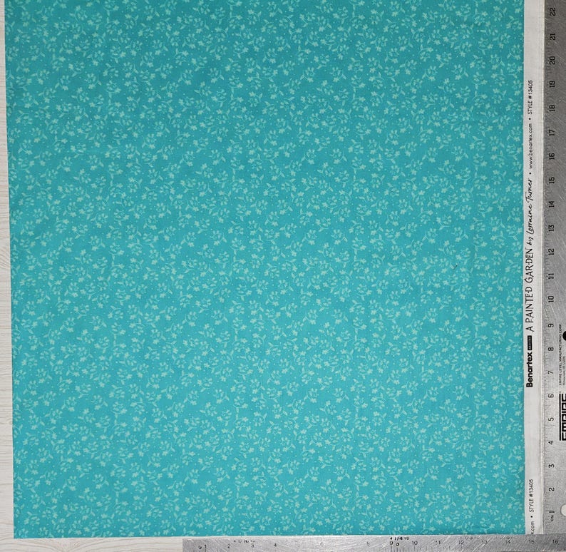 May include: Turquoise fabric with a repeating pattern of small, light green leaves. The fabric is labeled "A PAINTED GARDEN" by Lorraine Turner. The fabric is marked with measurements in inches.