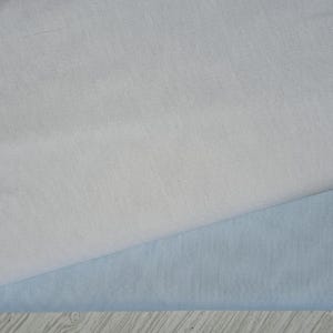May include: Two pieces of fabric, one light gray and one light blue, are folded over each other. The fabric is smooth and has a subtle sheen.