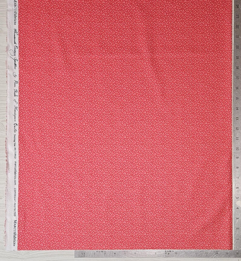 May include: A piece of red fabric with a repeating pattern of small, light red swirls. The fabric has a ruler along the right edge and text along the left edge that reads "MARCUSFabrics About Country Sparklers by Pam Buch of Hemstypu will swing VRITION marcusfabrics.com COPYRIGHT PROTECTED MARCUSFabricss."