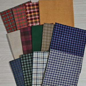 Puede incluir: Una colección de doce muestras de tela rectangulares dispuestas en abanico. El surtido incluye varios diseños textiles como amarillo mostaza sólido, verde oscuro sólido, beige liso y múltiples patrones de cuadros y vichy en rojo, azul, verde y negro.