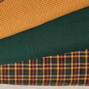 Puede incluir: Tres piezas de tela dobladas apiladas. La capa superior tiene un patrón de microcuadros en amarillo mostaza y blanco. La capa intermedia es de un verde bosque oscuro sólido. La capa inferior presenta un patrón de cuadros en negro, verde y rojo.