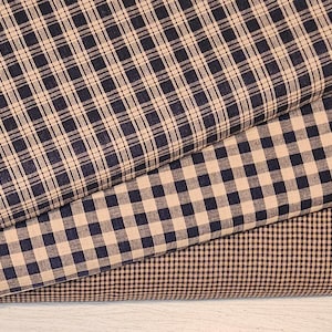 May include: Three pieces of fabric with different plaid patterns. The top fabric is a fine plaid with thin black and tan lines. The middle fabric is a larger plaid with thicker black and tan lines. The bottom fabric is a smaller plaid with thin brown and tan lines.