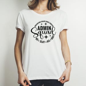 Może przedstawiać: Biała koszulka z czarnym kołem z napisem "Organizing Chaos Since Forever Admin Squad We Slay All Day".