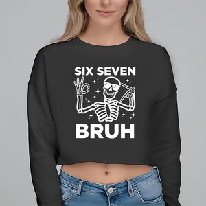 May include: Black cropped sweatshirt with the text "SIX SEVEN BRUH" and a white skeleton graphic wearing sunglasses and making hand gestures. The skeleton is surrounded by stars.