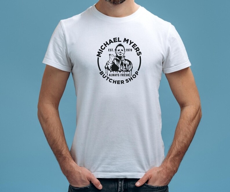 May include: White t-shirt with a black and white graphic of Michael Myers from the movie Halloween. The graphic is a circle with the text "Michael Myers Butcher Shop Est. 1978 Always Fresh" around the image of Michael Myers.