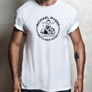 May include: White t-shirt with a black and white graphic of Michael Myers from the Halloween franchise. The graphic says "Michael Myers Butcher Shop Est. 1978 Always Fresh".