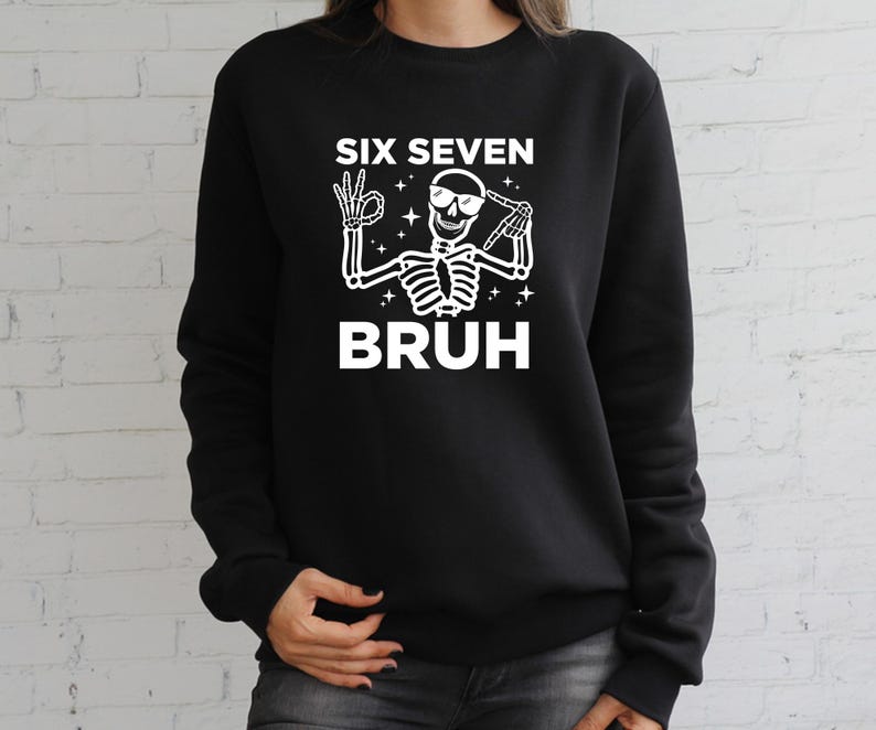 May include: Black sweatshirt with a white graphic of a skeleton wearing sunglasses and making hand gestures. The text "SIX SEVEN BRUH" is above and below the skeleton illustration. The sweatshirt is a casual style.