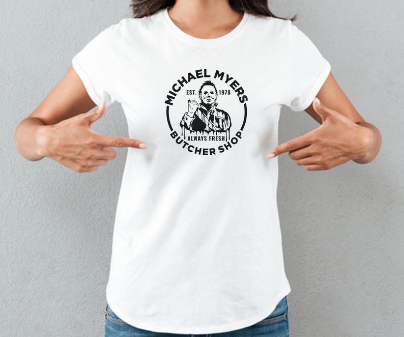 May include: White t-shirt with a black and white graphic of Michael Myers from the movie Halloween. The graphic says "Michael Myers Butcher Shop Est. 1978 Always Fresh".