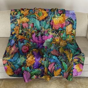 May include: A plush throw blanket featuring a vibrant, intricate floral pattern with swirling acanthus-style leaves. The design showcases a rich color palette of deep purple, bright orange, teal, magenta, and golden yellow against a dark background.