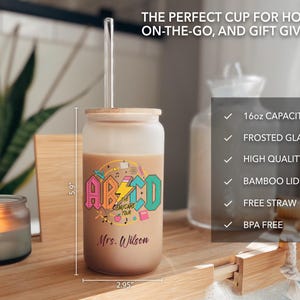 May include: A frosted glass 16 ounce tumbler with a colorful "ABCD Daycare Tour" graphic and the name "Mrs. Wilson" printed on it. The tumbler has a bamboo lid and comes with a clear plastic straw.