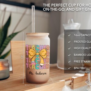 May include: A frosted glass 16 ounce tumbler with a bamboo lid and a clear straw. The tumbler has a colorful graphic of the word "Teacher" with a pencil and a bow. The tumbler is personalized with the name "Ms. Anderson".