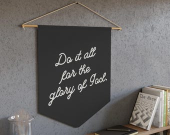 Puede incluir: Pancarta negra con texto blanco que dice "Do it all for the glory of God." La pancarta está colgada de una varilla de madera.