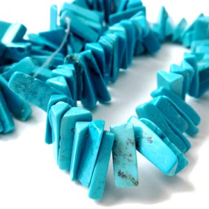 May include: A strand of turquoise-colored, rectangular beads. The beads are a vibrant blue-green hue, with some showing natural variations in color and texture. The beads are strung together, creating a necklace or bracelet.