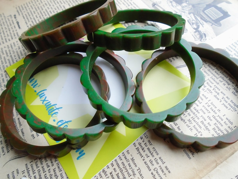 May include: A collection of vintage green and brown scalloped bangles. The bracelets are made of a mottled material, with a wavy edge design. The background includes vintage book pages and a yellow and green geometric shape.