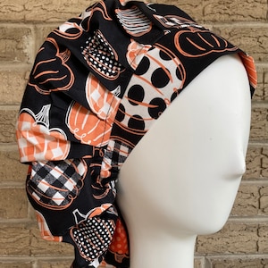 May include: Black scrub hat with a pumpkin print in orange and white. The hat has a gathered ruffle around the edge.