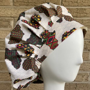 May include: A white surgical cap with a colorful African print design. The print features green, red, yellow, and black geometric shapes. The cap is made of a soft, comfortable fabric and is designed to be worn by healthcare professionals.