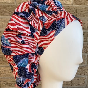 May include: A red, white, and blue patterned surgical scrub hat with a design of American flags. The hat is made of a soft, comfortable fabric and is perfect for nurses, doctors, and other healthcare professionals.