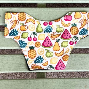 May include: White underwear with a colorful fruit pattern. The design includes illustrations of bananas, apples, grapes, lemons, cherries, pineapples, pears, and watermelon. The underwear has a black trim.