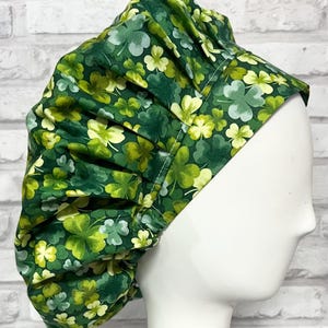 May include: A green and white clover print bouffant surgical scrub cap. The cap is made of fabric and has an elastic band. The cap is designed to cover the hair during medical procedures. The cap is a St. Patrick's Day theme.
