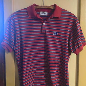Op de afbeelding: Rood en blauw gestreept poloshirt met korte mouwen. De kraag en manchetten zijn rood, met een klein geborduurd logo op de borst. De merknaam "Garan" is zichtbaar op de kraag.